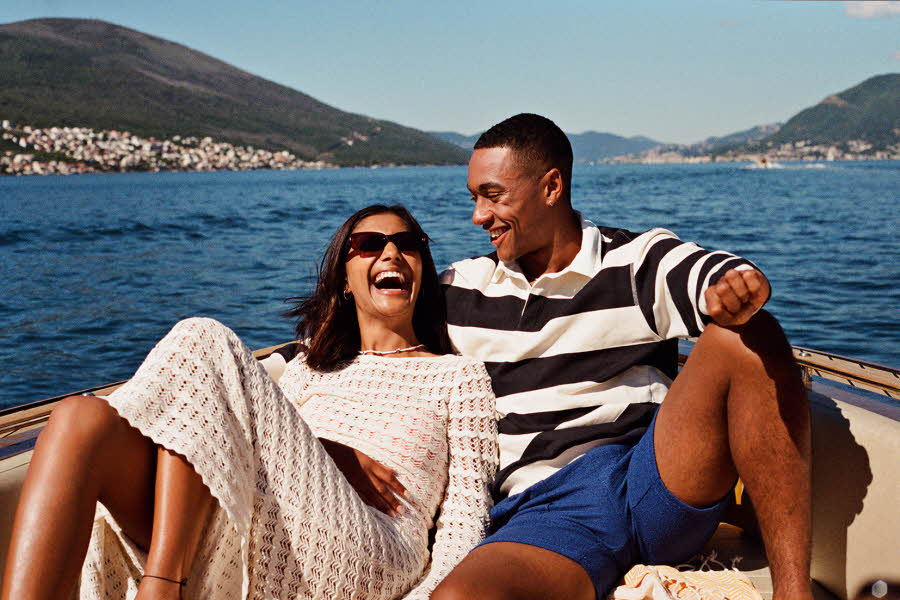 Par sitter foran på båt og smiler og ler i sola