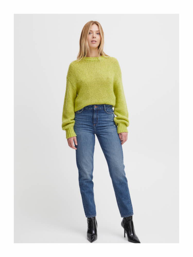 Damemodell med gulgrønn strikkegenser, jeans og sorte støvletter
