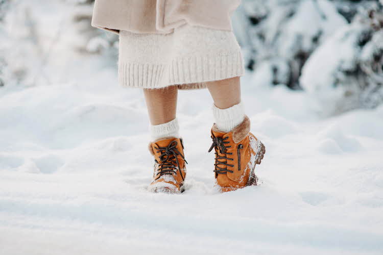 Dame som står i snøen med oransje foret vintersko