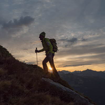 Mann går med stav i solnedgangen opp et fjell
