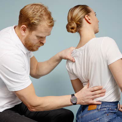Mann kiropraktor som presser en dame i ryggen med hånden sin
