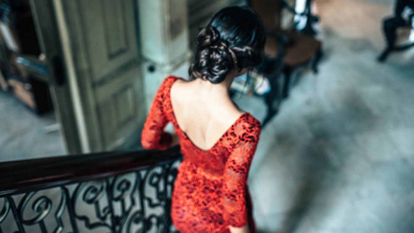 Ryggen til dame i rød kjole og oppsatt hår som går ned en dekorativ trapp