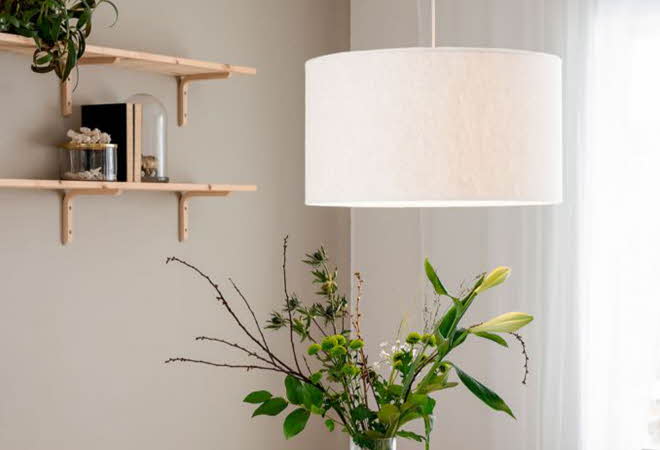 Hjørnet av et rom med en taklampe som henger over en vase med blomster, og et par hyller på veggen