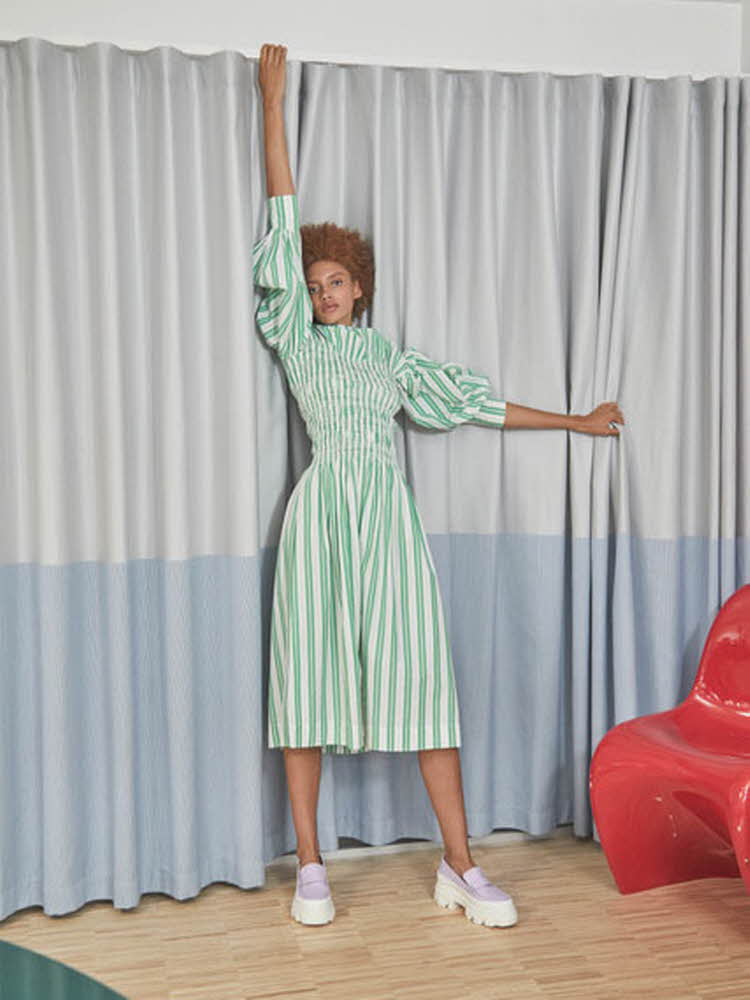 kvinnelig modell foran gardine, iført hvit og grønn stripete kjole