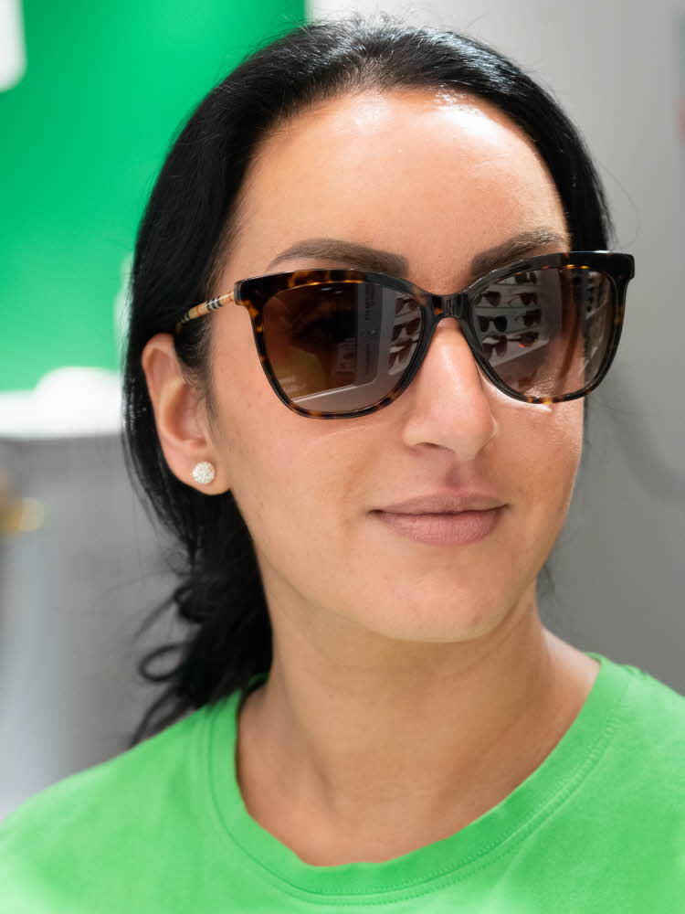 Jente med mørk hår og grønn genser, haar på seg en mørkebrun solbrille fra Burberry