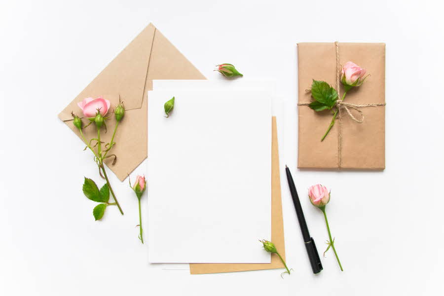 Flat lay av hvit ark omringet av brune kort og rosa roser
