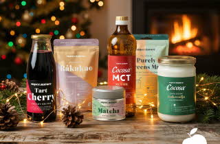 Supernature-produkter som kakao, matcha, kokosolje og MCT-olje plassert på bord med julelys og peis i bakgrunnen.