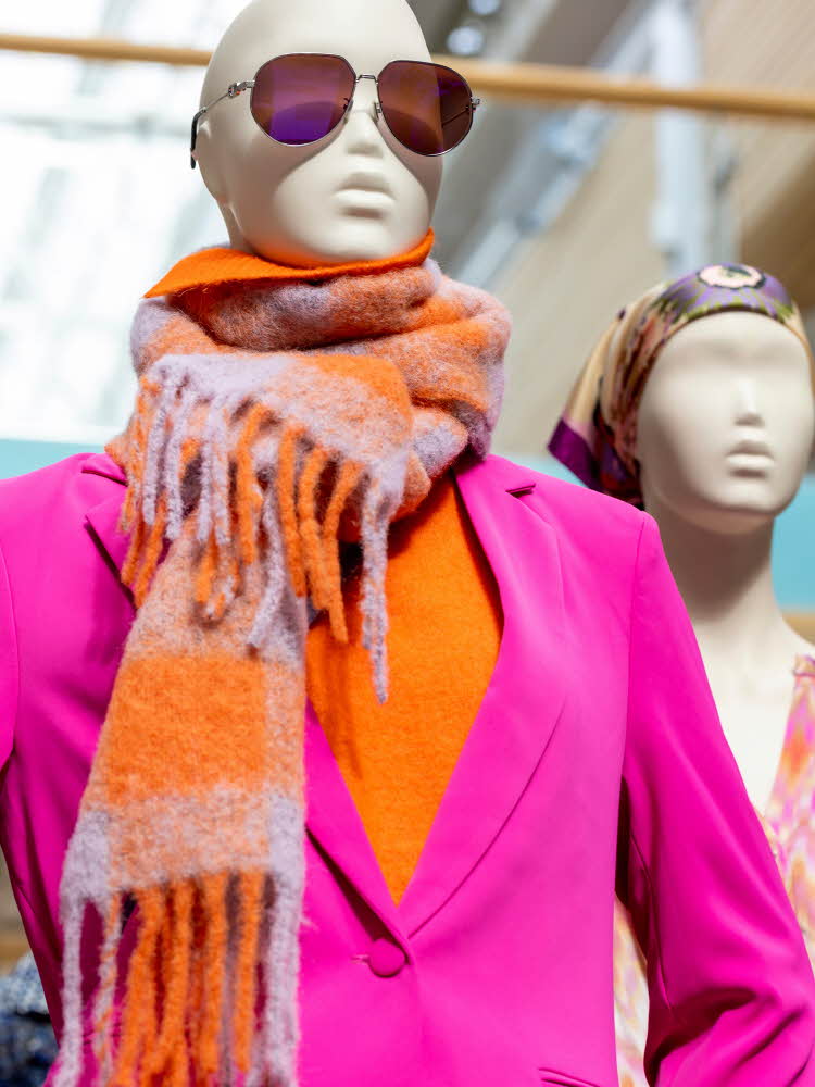 Halvfigurbilde av utstillingsdukke med solbriller, fargerikt skjerf, oransje topp og rosa dressjakke
