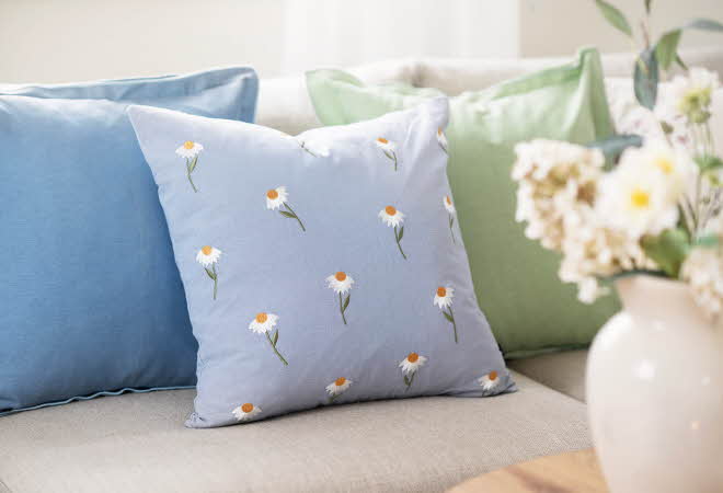 Tre pynteputer i blå og grønn på en sofa, med en vase med blomster i forgrunnen