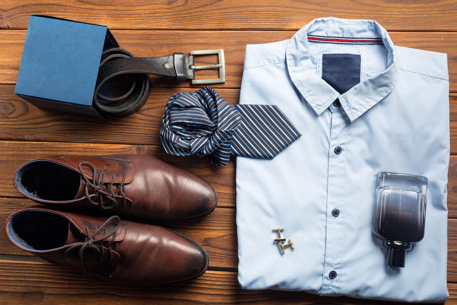 Pensko, belte, slips, skjorte, mansjetter og parfyme ligger fint lagt frem på en brun bordplate. Foto til artikkel om 10 gavetips til farsdag.