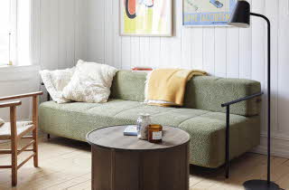 En stue med en grønn sofa, en lenestol, et stuebord og en gulvlampe