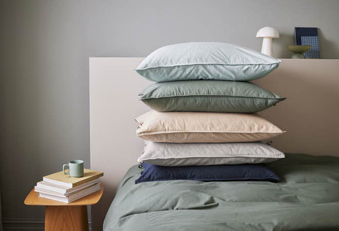 En seng med en stabel med puter i forskjellige farger.