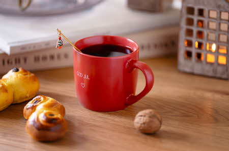rød kopp med kaffe og med gull tekst "god jul" og gull skje med julepynt omringet med lussekatt