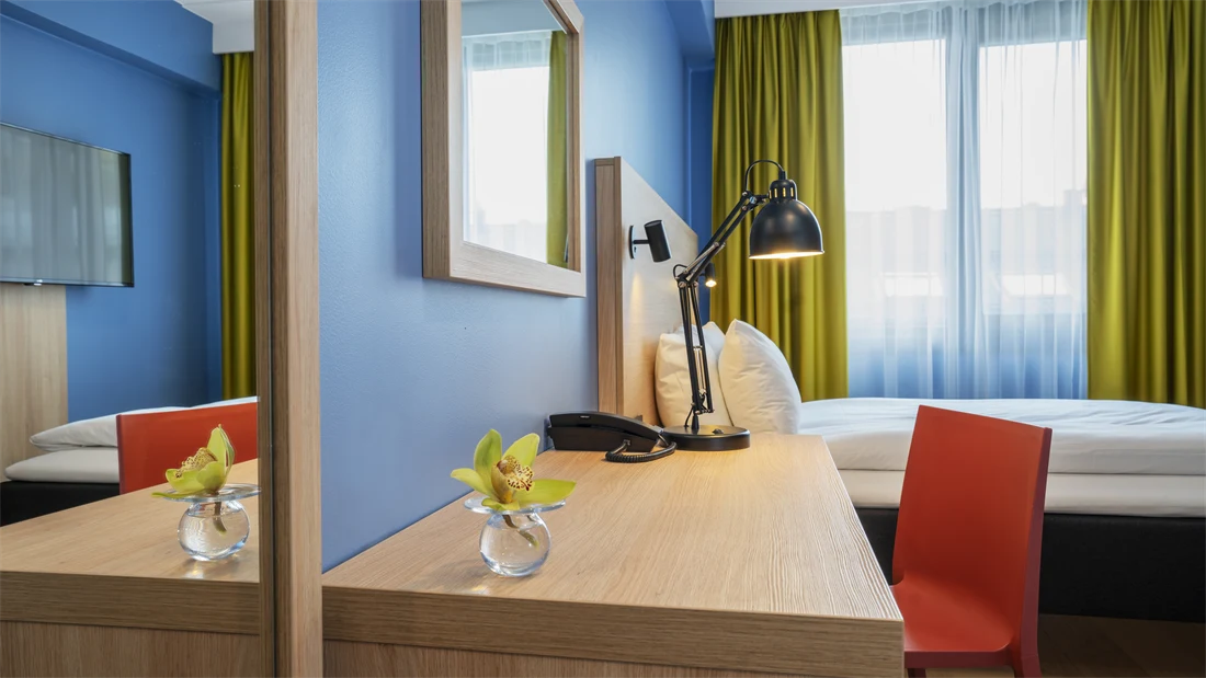 Speil. skrivebord med rød stol, blå vegger, dobbeltseng og gule gardiner i dobbeltrom på Thon Hotel Astoria