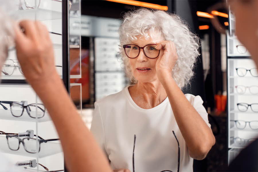 eldre dame som prøver på seg briller foran speilet