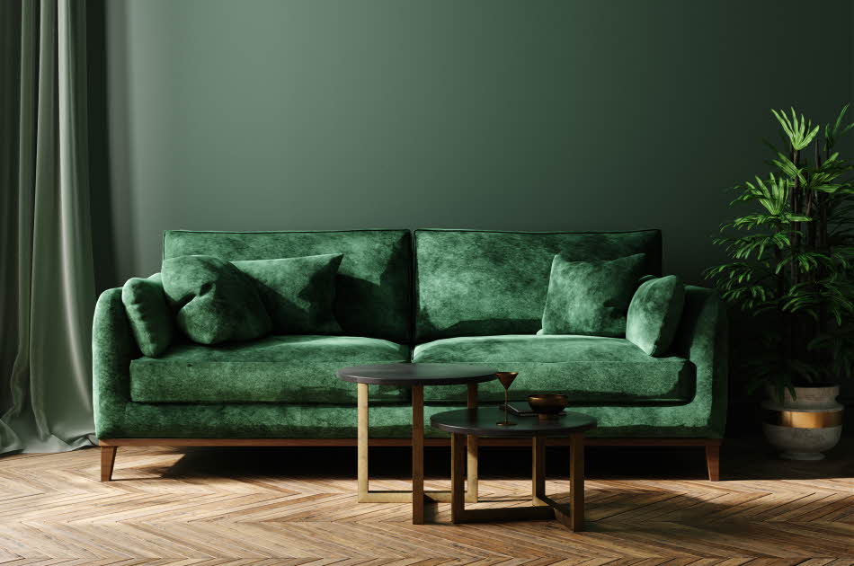Mørkegrønn vegg med en matchende mørkegrønn sofa i fløyel, samt to små bord