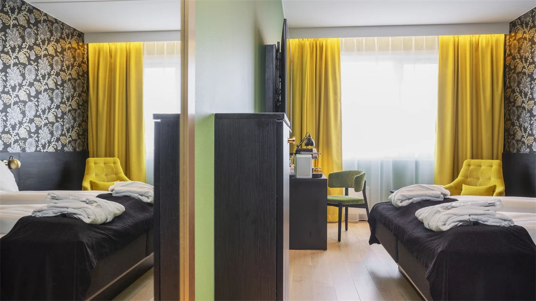 Stort speil, grønn vegg, skrivebord med stol, gule gardiner, gul stol og morgenkåper på sengen i superior rom på Thon Hotel Kirkenes