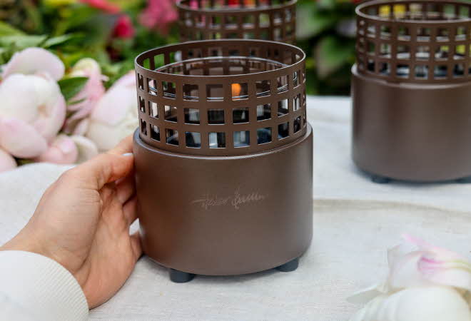 En hånd holder på en lykt fra Tenderflame som står på en bord