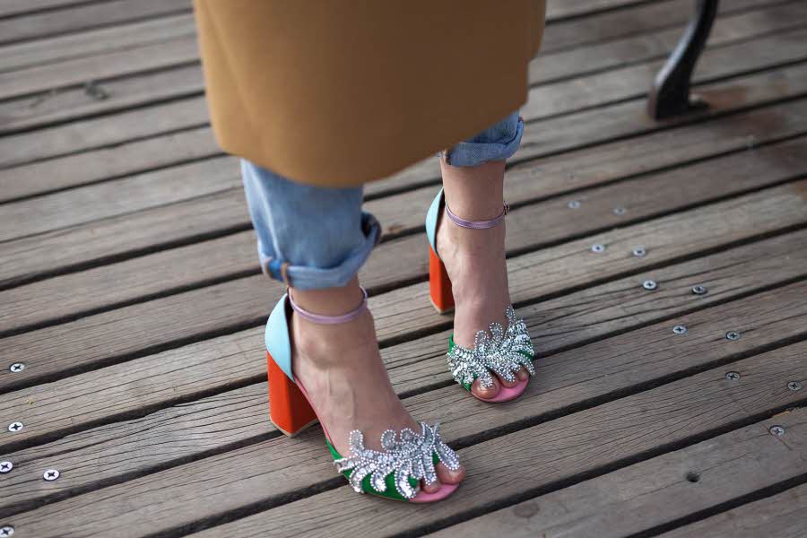 Nærbilde av et par dameføtter i høyhælte sandalpumps med glitter, strass, rød hæl og lyseblå detaljer. Illustrasjonsbilde til artikkel om vårmote for sko.