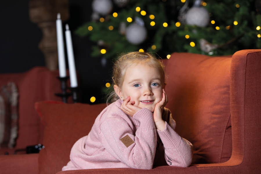forventnigsfullt barn i rosa ulldress foran juletre
