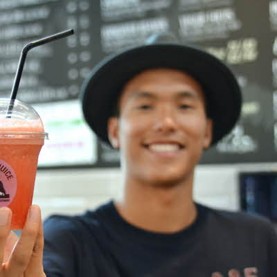 Smilende mann med sort hatt som holder en oransje juice med sugerør