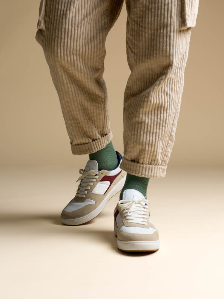 mann i lysebrun jakke, grønn skjorte og hvit bukse hvit velourbukse, grønne sokker og hvite, beige og røde sneakers