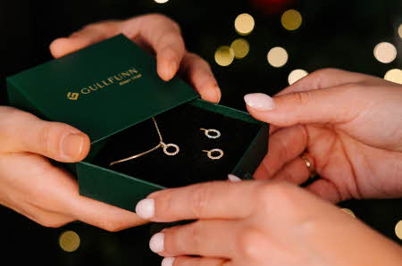 Nærbilde av et par hender som gir et annet par hender en boks med et smykkesett.