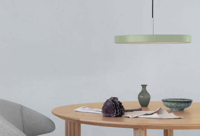 Et bord med en stol, som har en rund, flat lampe som henger fra taket over det