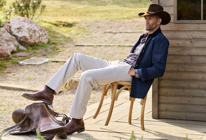 En mann i cowboy hatt sitter i en stol ute med en av føttene hans på en sal