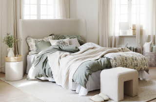 En seng i et soverom redd opp med hvitt og grønt sengetøy
