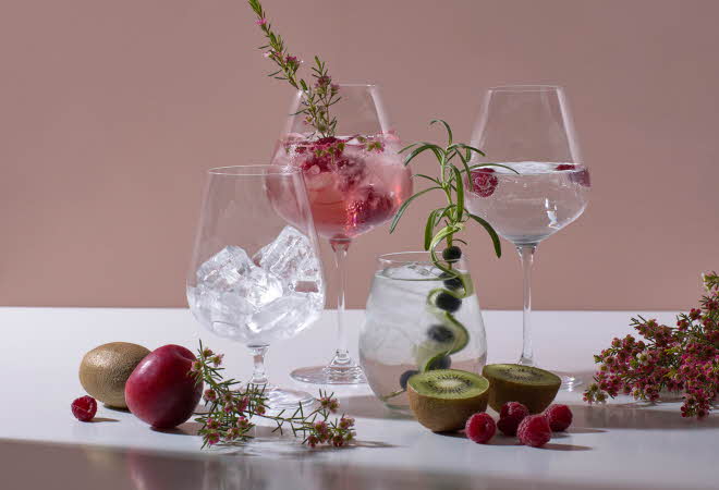 Tre glass med is og frukt på en hvit overflate mot en rosa bakgrunn.