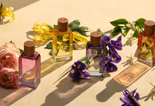 Fem parfymeflasker med trelokk omgitt av fargerike blomster.