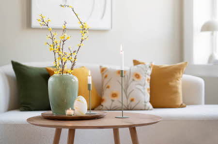 En sofa med pynteputer og et stuebord med vase og lysestaker