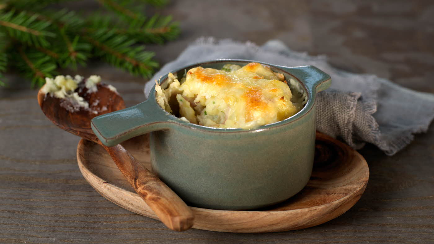 Ildfast grå porsjonsform med gratinert ost på et trebrett med en tresleiv ved siden