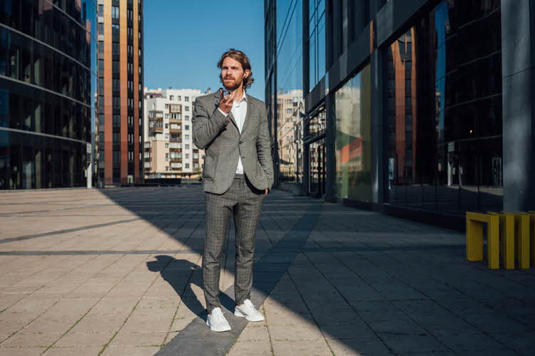 Mann kledd i grå dress, rutete bukse og hvite sneakers