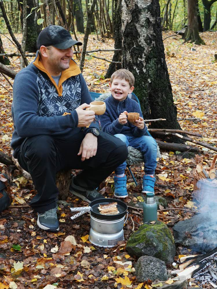Mann og barn som drikker varm drikke ved et bål i skogen