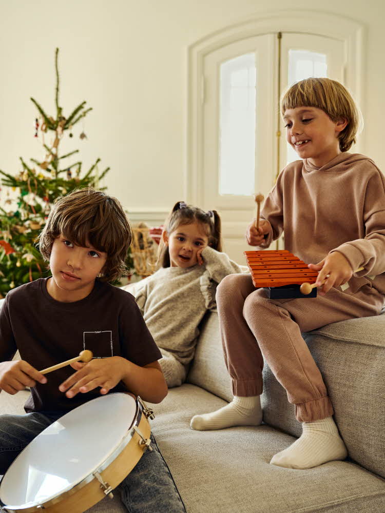 Barn som løper i en julepyntet stue Barn som leker med musikkinstrument på en sofa Jente i kjole Barn som lener seg på en vegg