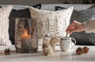 En hånd som rører i en kopp som står på et bord pyntet til vinter.