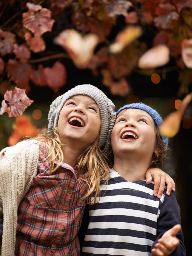 to barn som ser opp mot fallende høstblader med høstklær