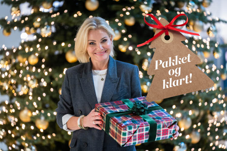 Dame med en innpakket julegave foran et juletre.