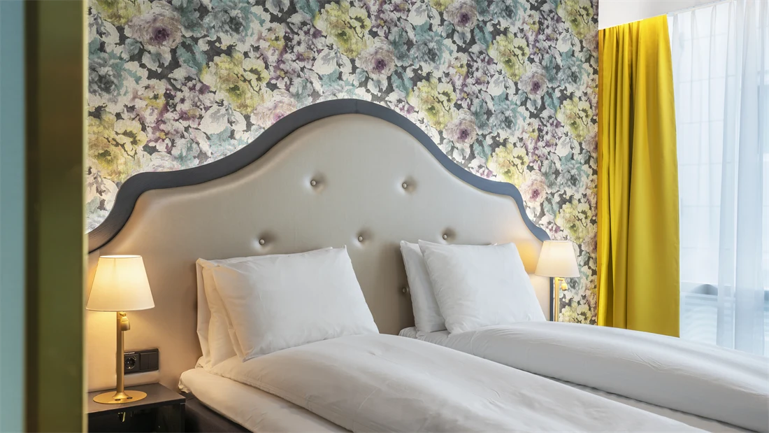 Dobbeltseng med sengegavl, blomstrete tapet og gule gardiner i dobbeltrom på Thon Hotel Cecil