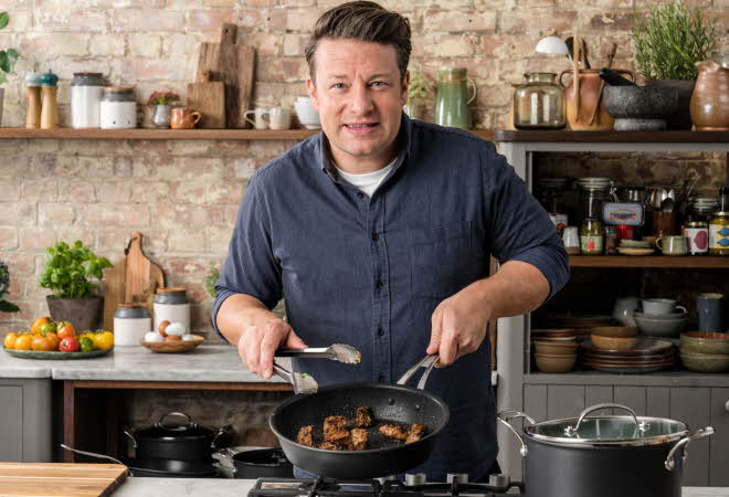 Jamie Oliver som står i et kjøkken og lager mat i en stekepanne