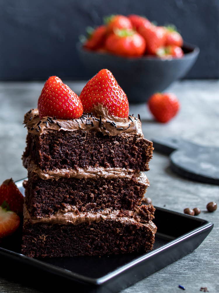 Et stykke  sjokoladekake i tre lag med jordbær på toppen
