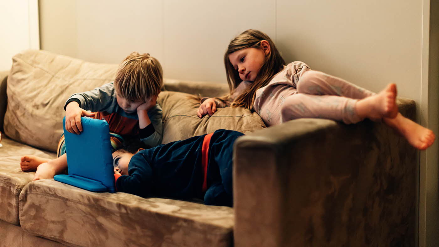 Tre trøtte barn ser film i sofa.