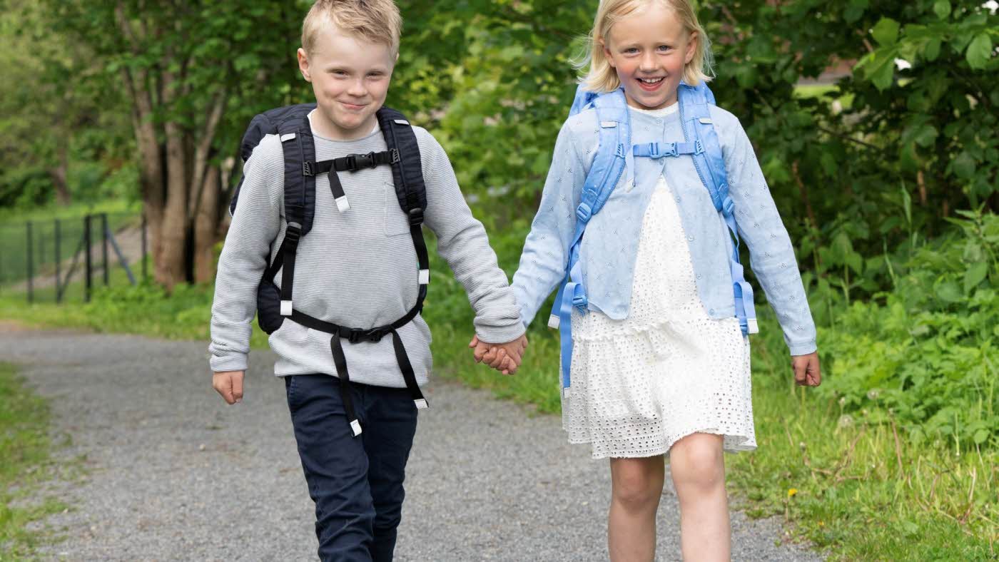 En gutt og en jente som går p åen grusvei, holder hender og har skolesekker på ryggen