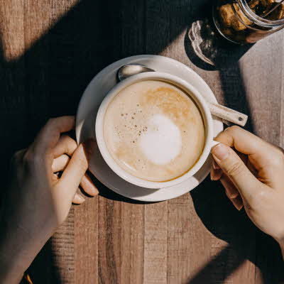 Kaffe latte i hvit kopp med to hender rundt på trebord