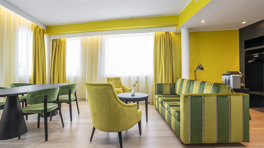 Sittegruppe med gul og grønn stripete sofa, rundt bord, gule stoler, spisegruppe med mørkt rundt bord og grønne stoler, gule vegger og gule gardiner i suite på Thon Hotel Kirkenes