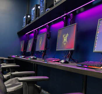 PC-skjermer på en rekke i et rom med lille LED-lys på veggen bak. Foto.