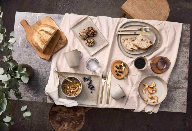 Et bord sett ovenfra dekket med Aida RAW servise, brød, bær og frokostblanding