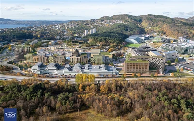 Illustrasjon viser et flyfoto av eksisterende Åsane sentrum, hvor nye planlagte bygninger er tegnet inn i grønt.